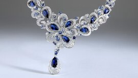 Close-up of a delicate silver necklace with numerous dark blue teardrop-shaped gemstones set into it.