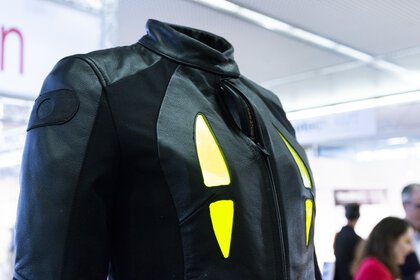 Nahaufnahme einer schwarzen Lederjacke mit lechtenden gelben Akzenten, die an einem Messestand ausgestellt ist.