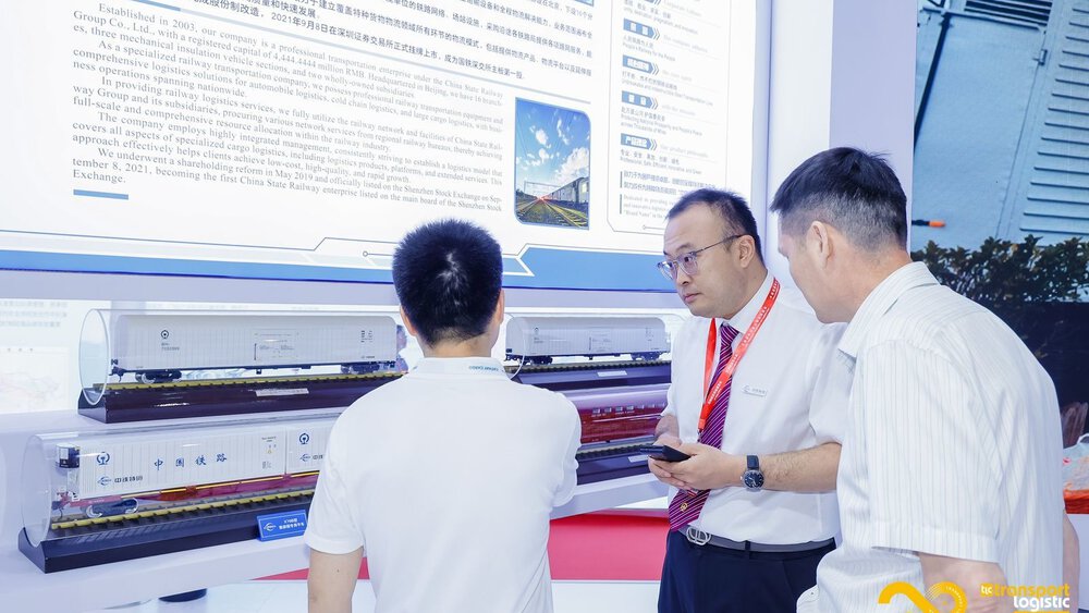 Three men in business attire talk in front of train models at a stand at 