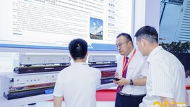 Three men in business attire talk in front of train models at a stand at 