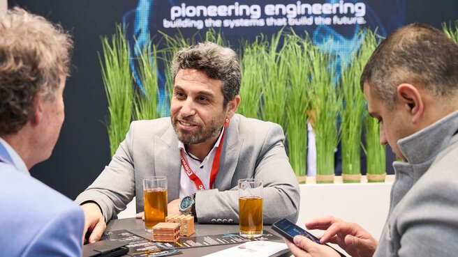 Three trade fair visitors are having a conversation at a table.