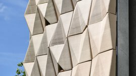 Modern building facade with geometric, three-dimensional beige panels against a blue sky.
