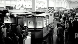 Schwarz-weißes Foto von einer früheren productronica. Menschen laufen durch eine Halle, in der diverse Messestände aufgebaut sind.