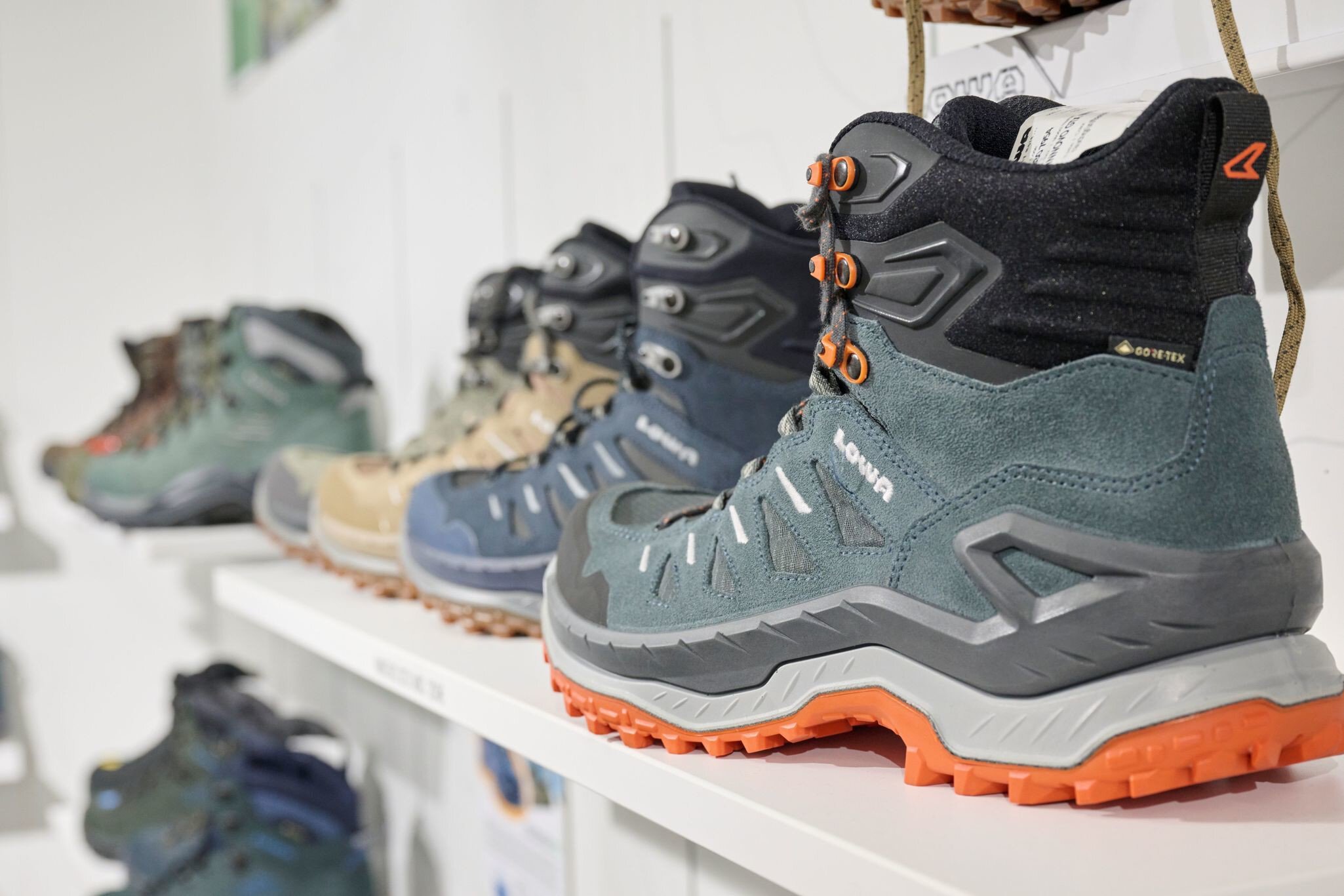 Nahaufnahme von Wanderschuhen in verschiedenen Farben, die in einem Geschäft auf weißen Regalen ausgestellt sind.