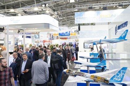 An exhibition stand with several aeroplane models, which numerous trade fair visitors walk past.