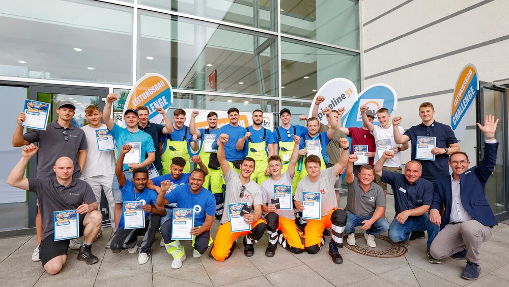 Gruppe von Teilnehmenden posiert vor einem Gebäude mit Urkunden in der Hand, im Hintergrund Banner mit der Aufschrift ‚Leitungsbau Challenge‘