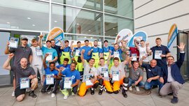 Gruppe von Teilnehmenden posiert vor einem Gebäude mit Urkunden in der Hand, im Hintergrund Banner mit der Aufschrift ‚Leitungsbau Challenge‘