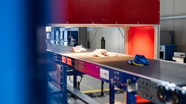 Ein Förderband mit Textilien läuft durch einen optischen Sensor beim Textilrecycling.