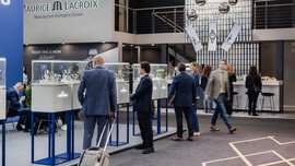 Several trade fair visitors are standing at the INHORGENTA stands, looking at various watch models on display in glass showcases.