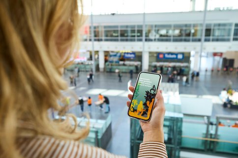 Frau blickt in der Messehalle auf ihr Smartphone mit einer Grafik zur nachhaltigen Wald- und Zukunftsgestaltung.