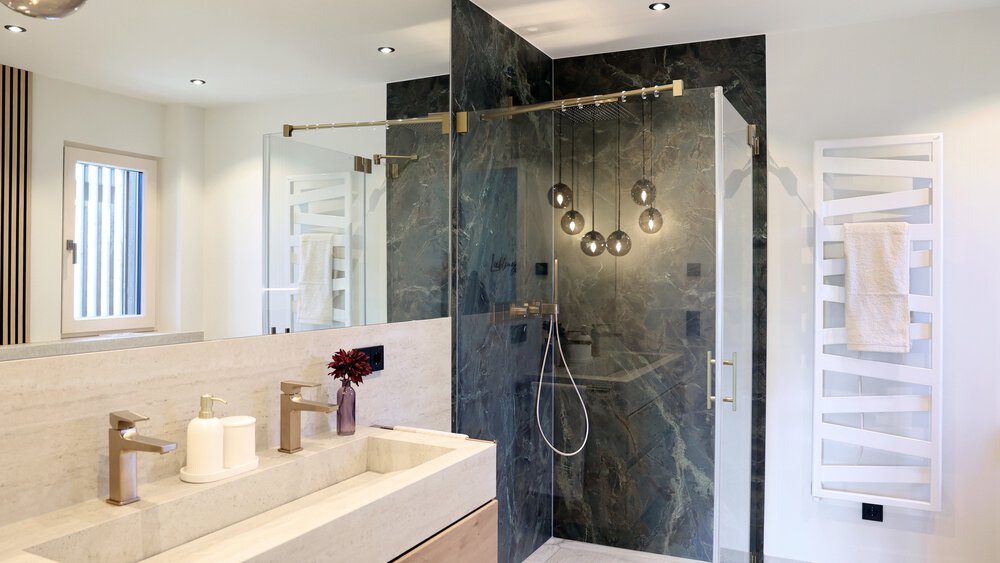 Modernes Badezimmer mit Doppelwaschbecken, Glasdusche mit dunkler Fliesenwand und Handtuch auf einem weißen Handtuchwärmer.