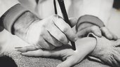 Sharp white photo of a person holding a medical device in the form of a pen to the hand of another person.