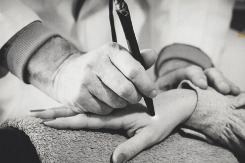 Sharp white photo of a person holding a medical device in the form of a pen to the hand of another person.