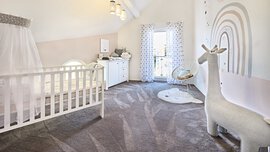 Das KAMPA-Kinderzimmer verfügt über ein gemütliches Kinderbett mit Baldachin, eine elegante Kommode und ein süßes Giraffenspielzeug unter einem farbenfrohen Regenbogen-Wandbild.