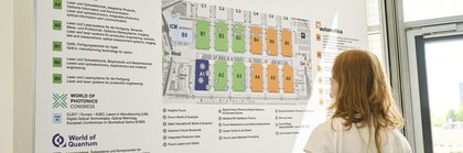 Person steht vor einem großformatigen Geländeplan der Messe München mit Hallenübersicht und Informationen zu mehreren Fachmessen und liest die Angaben.