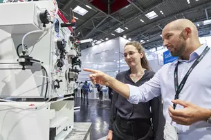 Two people examine a machine at an industrial trade fair.