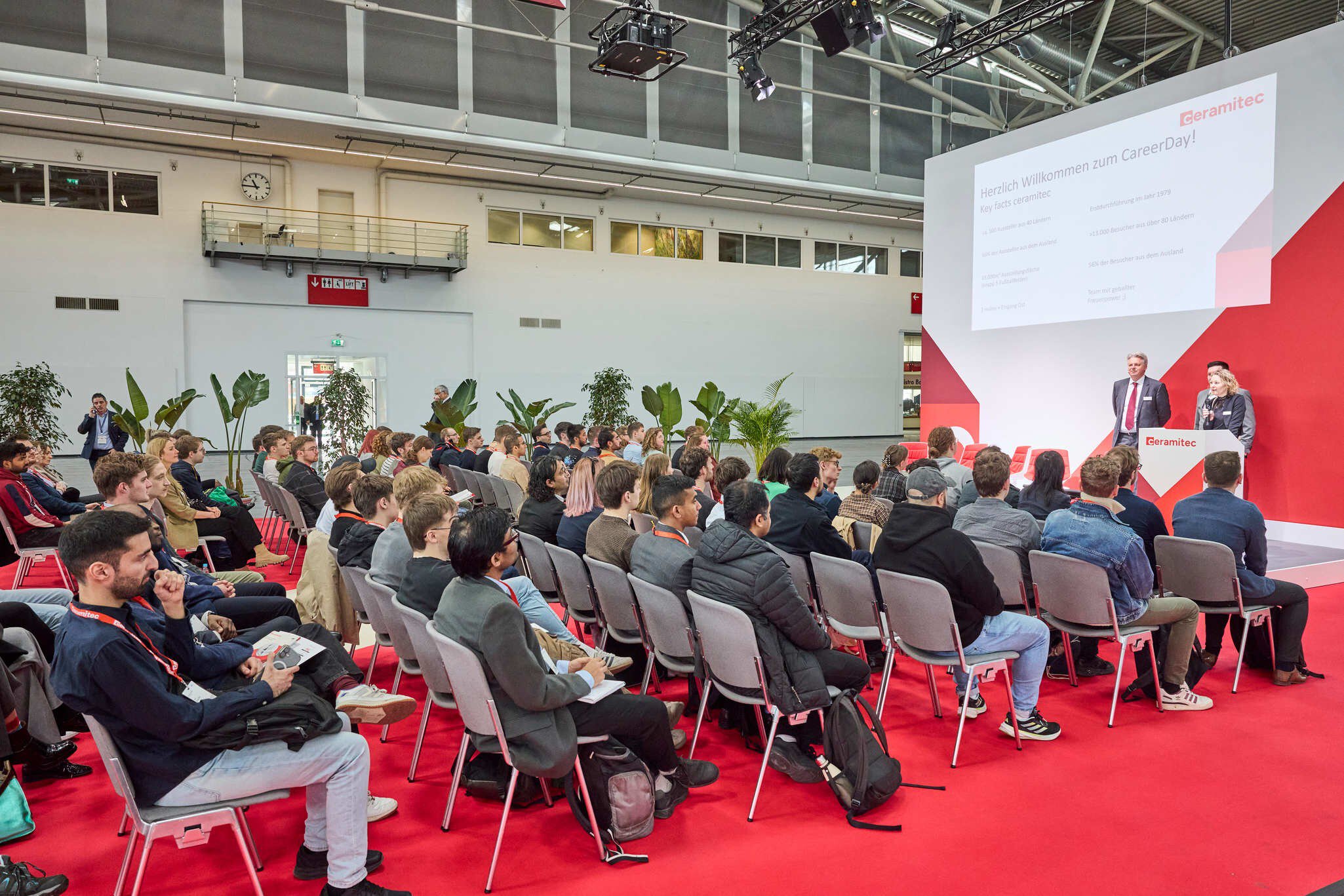 Ein gut besuchter Vortrag auf einer Messebühne, bei dem Referenten ein Publikum über Karrieremöglichkeiten und Brancheninformationen informieren.