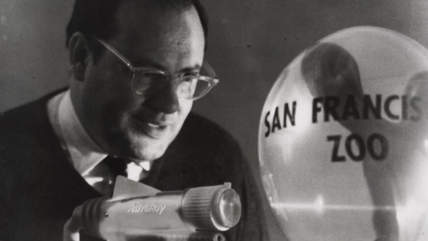 Schwarzweißfoto von einem Mann, der einen Laser auf einen Ballon mit der Aufschrift 