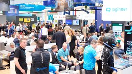 Numerous visitors at transport logistic Americas sit together in groups. Above the photo a banner with information about the trade fair, such as the date, location, etc.
