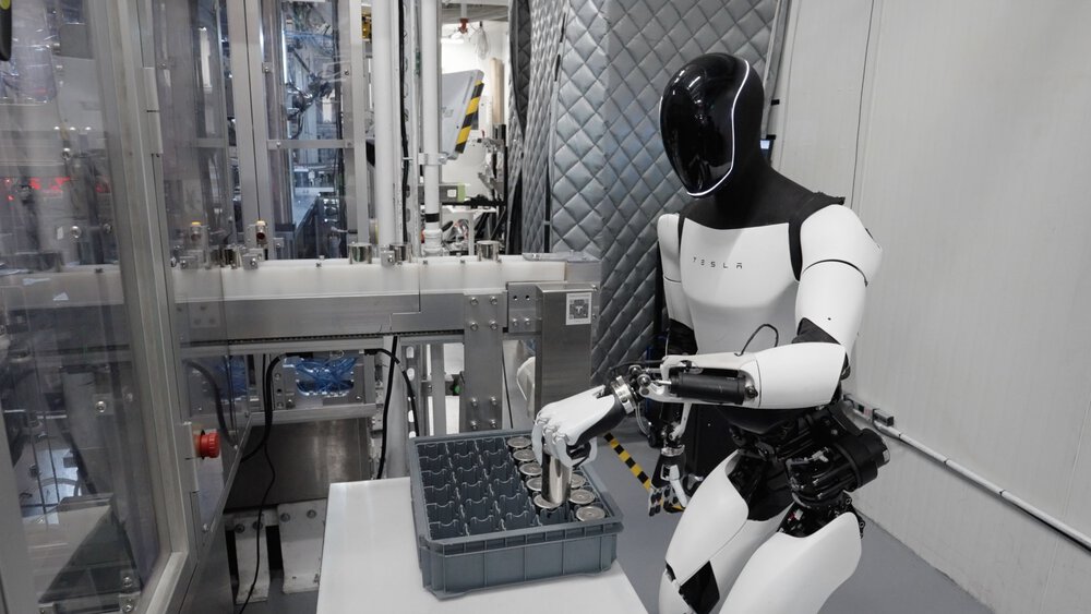 In einer Laborumgebung sortiert ein weißer humanoider Roboter Metallzylinder in eine Kiste.