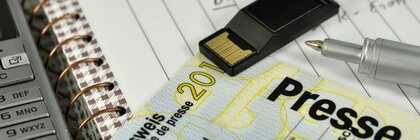 Ein Presseausweise auf einem Schreibtisch mit einem Notizblock und anderen Utensilien.