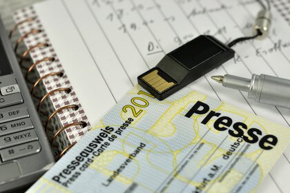 A press pass on a desk with a notepad and other paraphernalia.