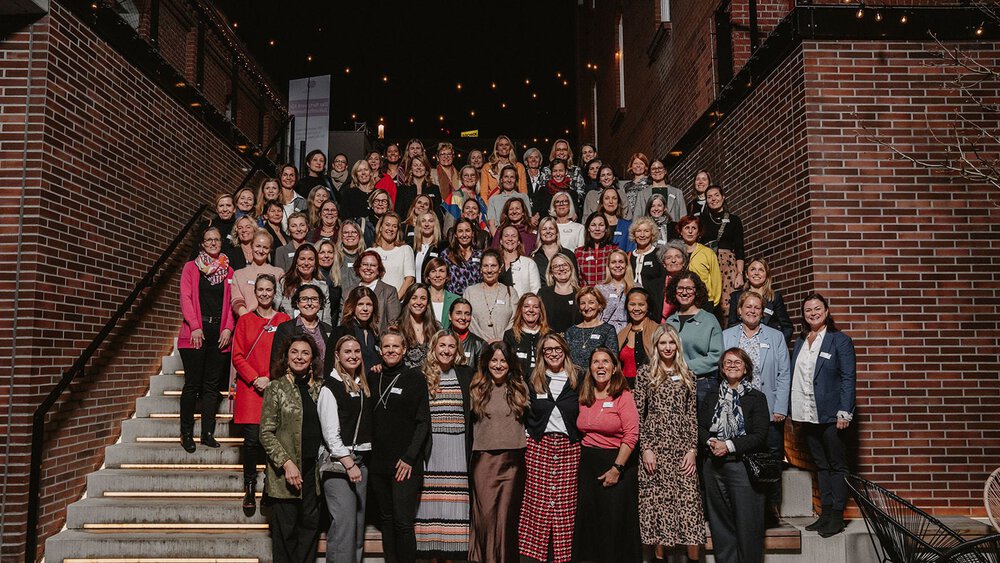 Eine große Gruppe von Frauen von „Frauen Verbinden“ steht auf einer Treppe im Freien und lächelt strahlend für ein Gruppenfoto