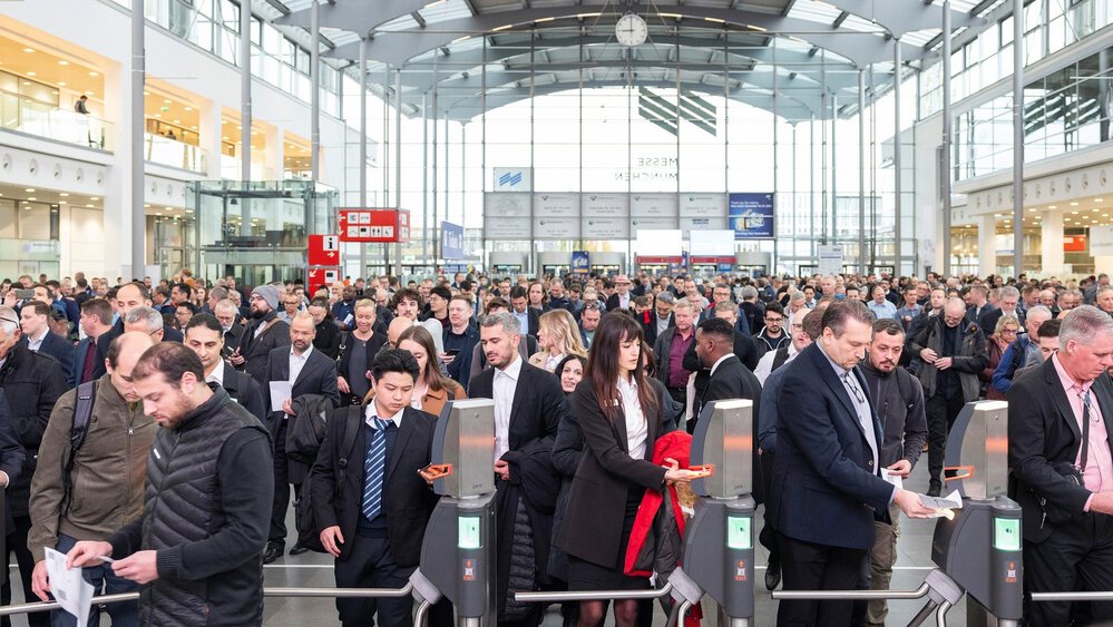 Numerous visitors queue in the entrance hall of productronica to scan their tickets at the turnstiles and enter.