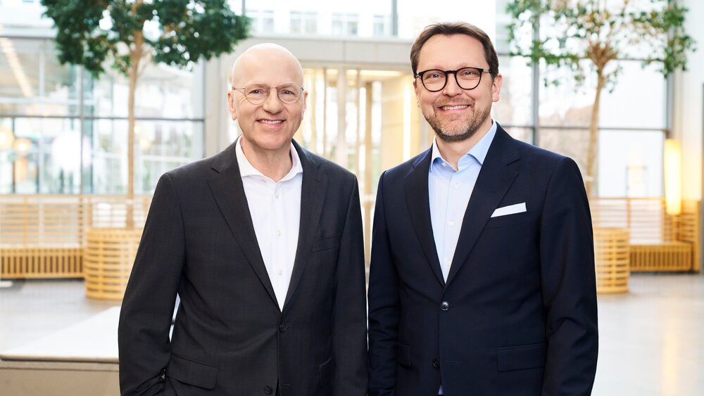 The photo shows two gentlemen, the CEOs of Messe München, both wearing black suits.