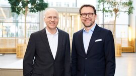 The photo shows two gentlemen, the CEOs of Messe München, both wearing black suits.