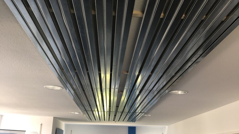 An der Decke montierte Metallschienen mit eingefädelten Schläuchen, in einem modernen Ausstellungsraum.