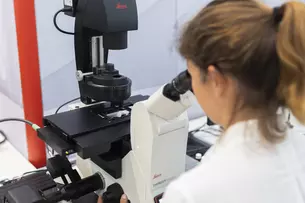 A person in a lab coat looks through a microscope.