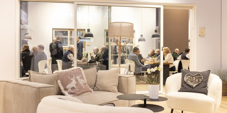 Gemütlicher Loungebereich mit Sofas und Kissen im Vordergrund, dahinter Tagungsraum mit mehreren Personen bei Gesprächen und Meetings an Tischen.