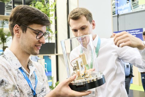 Two young men look with great interest at a technical exhibit in a glass display case at the World of Quantum in Munich.