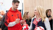 The athlete presents signed soccer balls to a visitor and chats with her at the exhibition stand.