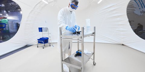 Ein Mann in weißer Laborkleidung steht an einem Metallwagen in einem weißen Laborzelt auf der productronica.