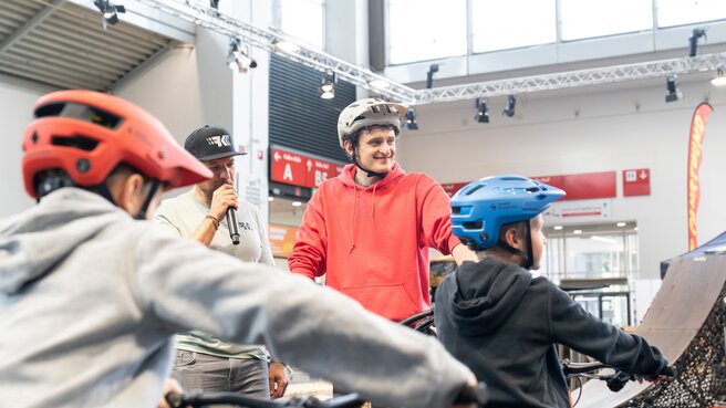 Radfahrer und Zuschauer bei einer Fahrradveranstaltung in einer Halle.
