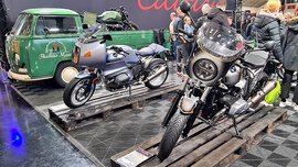 Bild von zwei älteren Motorrädern und einer grünen Ape in einer Messehalle.