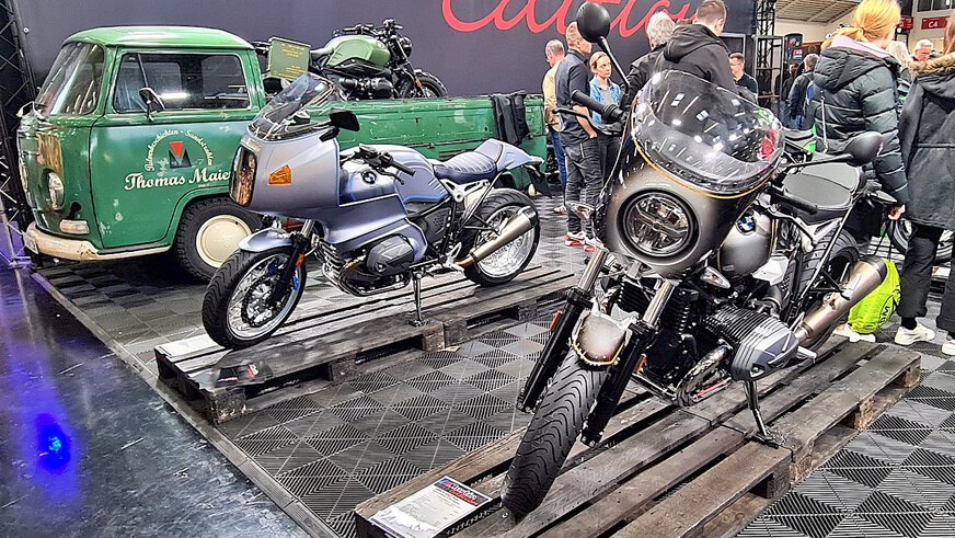 Picture of two older motorcycles and a green Ape in an exhibition hall.