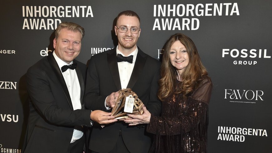 Three smiling people hold the trophy for the “Design Newcomer of the Year” category in front of a logo wall at the INHORGENTA AWARD Gala.