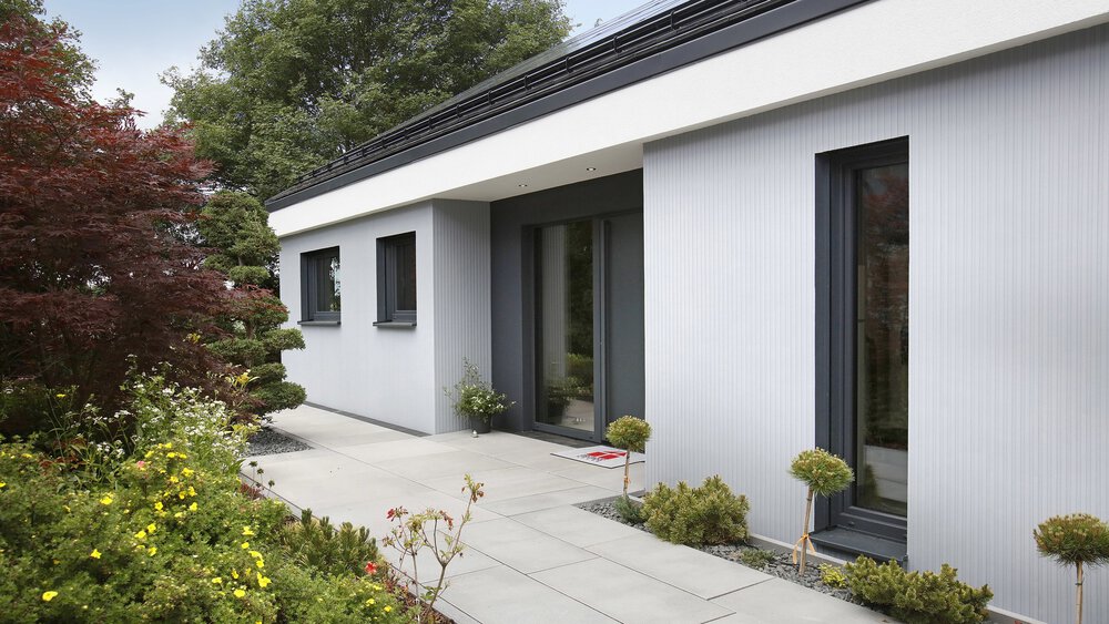 Modernes weißes Haus mit großen Fenstern, umgeben von einem üppigen Garten und einem Vorweg.