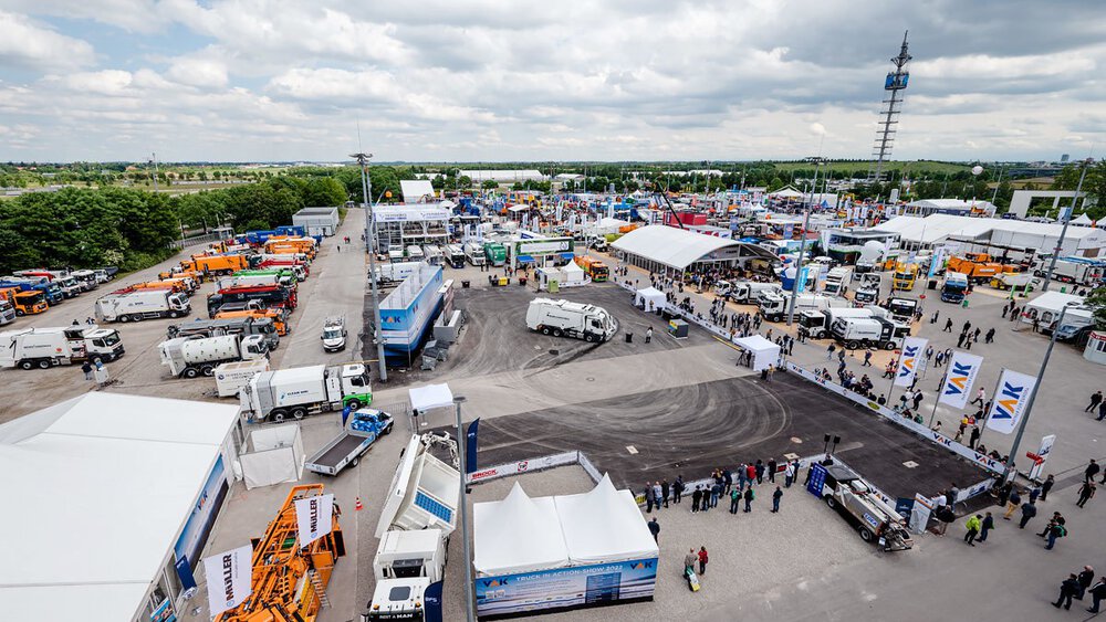 Luftaufnahme der Outdoor-Ausstellungsfläche mit Nutzfahrzeugen, Maschinen und Demonstrationsbereichen für Umwelttechnologien, Recycling und Wasserstofflösungen. Besucher erkunden Stände und Innovationen unter freiem Himmel.