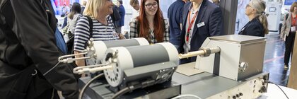 Several people are talking around the electrical appliances on display at an exhibition stand.