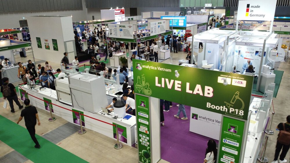A lively exhibition hall with various stands and a large green LIVE LAB sign at analytica Vietnam.