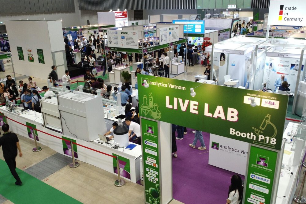 A lively exhibition hall with various stands and a large green LIVE LAB sign at analytica Vietnam.