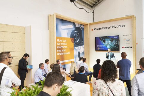 Ein Vortragender steht auf der Bühne der Fläche Machine Vision Pavilion und einige Fachbesucher hören bei seinem Vortrag zu