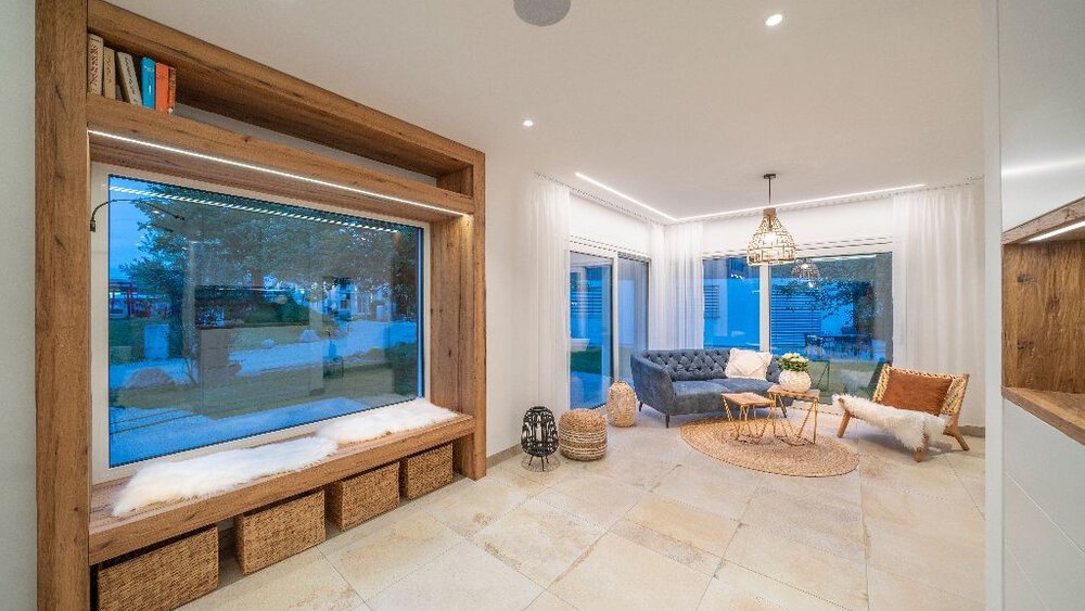 Modernes Wohnzimmer mit großer Fensterbank, Weidenkörben, blauem Sofa und rundem Couchtisch.