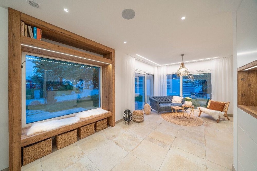 Modernes Wohnzimmer mit großer Fensterbank, Weidenkörben, blauem Sofa und rundem Couchtisch.