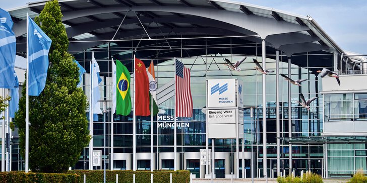 Gebäude vom Eingang West des Messe München Geländes mit Messesee und mehreren Flaggen an Fahnenmasten, z.B. USA, China & Indien.