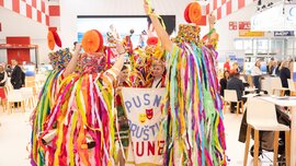 Gruppe von Menschen steht im Kreis umhüllt von bunten Luftschlangen aus Krepppapier